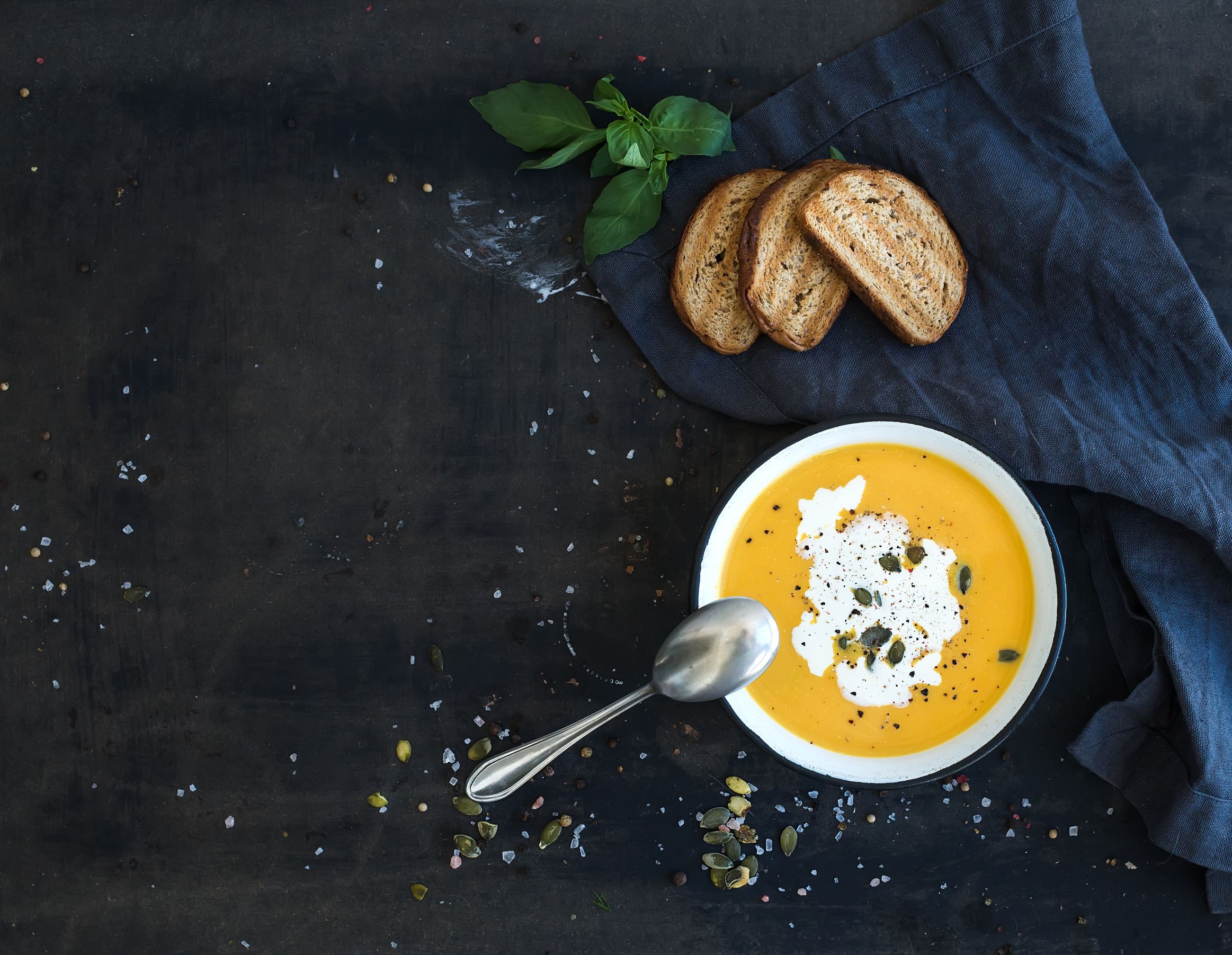 40578087 - pumpkin soup with cream, seeds, bread and fresh basil in rustic metal plate on grunge black background. top view, copy space